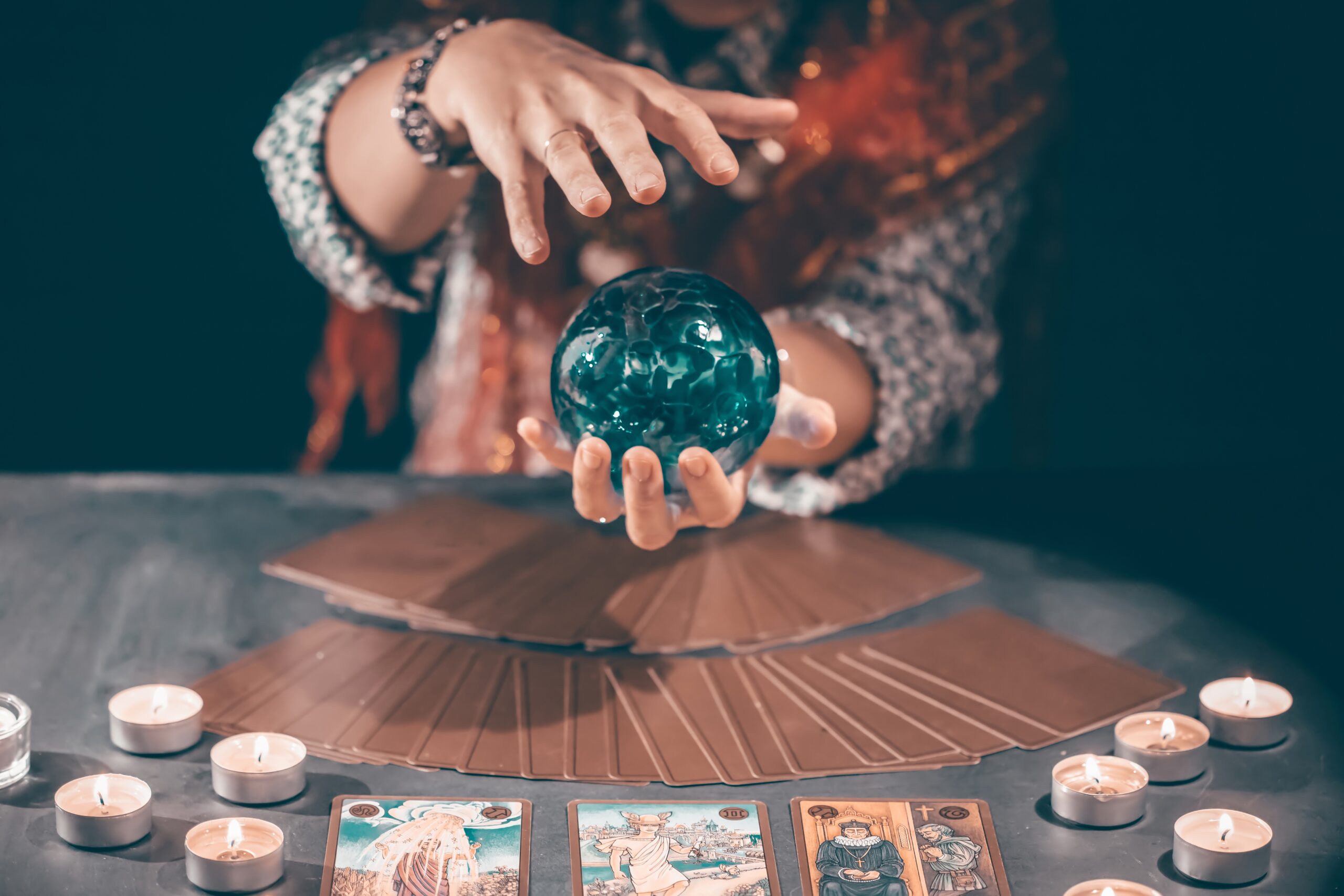 Fortune teller with tarot cards on table near burning candles.