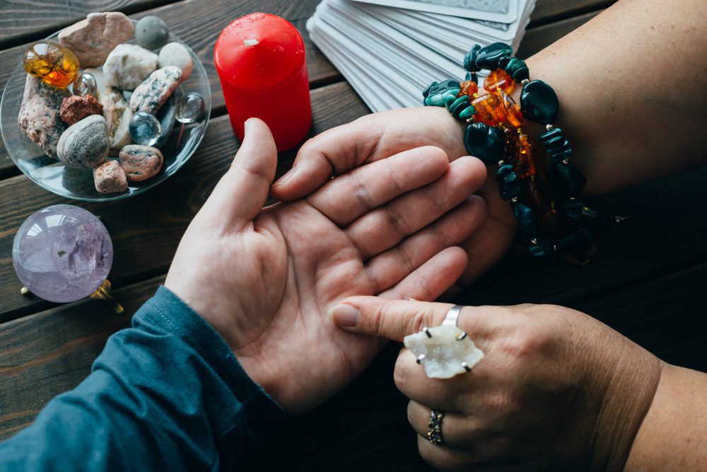 Palmistry fortune teller reads lines on man hand or palm to tell his future, top view, toned