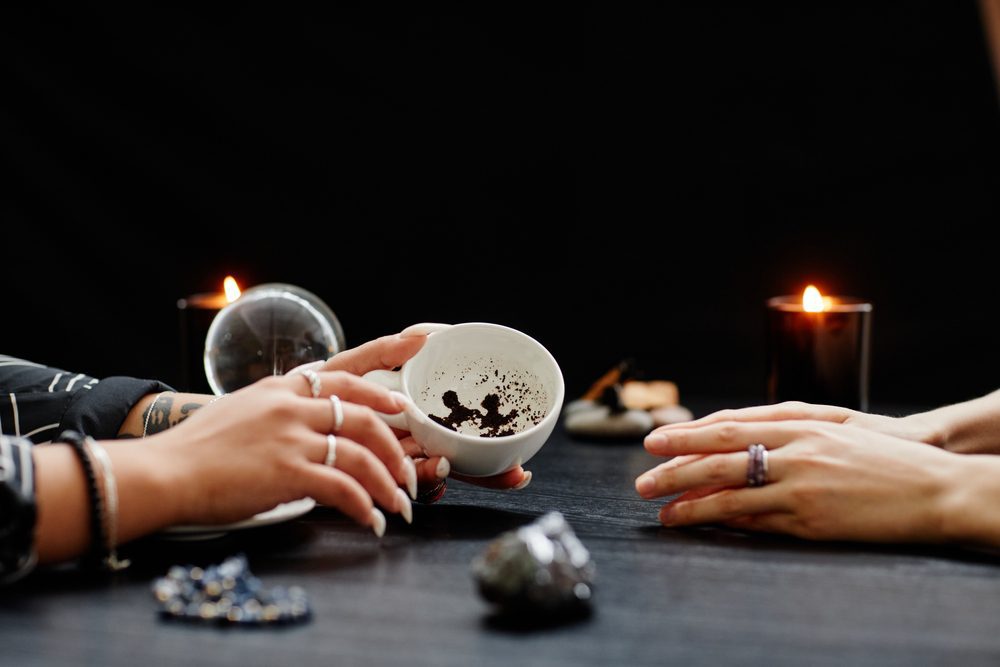 Side view close up of female fortune teller reading coffee grounds telling destiny in seance with young woman in dark