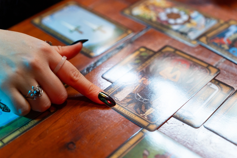 Fortune teller pointing at the devil card while interpreting a spread of tarot cards on a rustic wooden table, revealing insights into the future